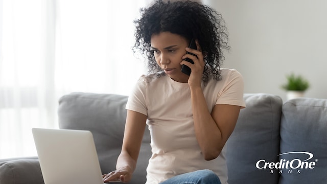 A woman looks at her laptop with a concerned expression as she talks on the phone, possibly trying to deal with a missing credit card payment. 