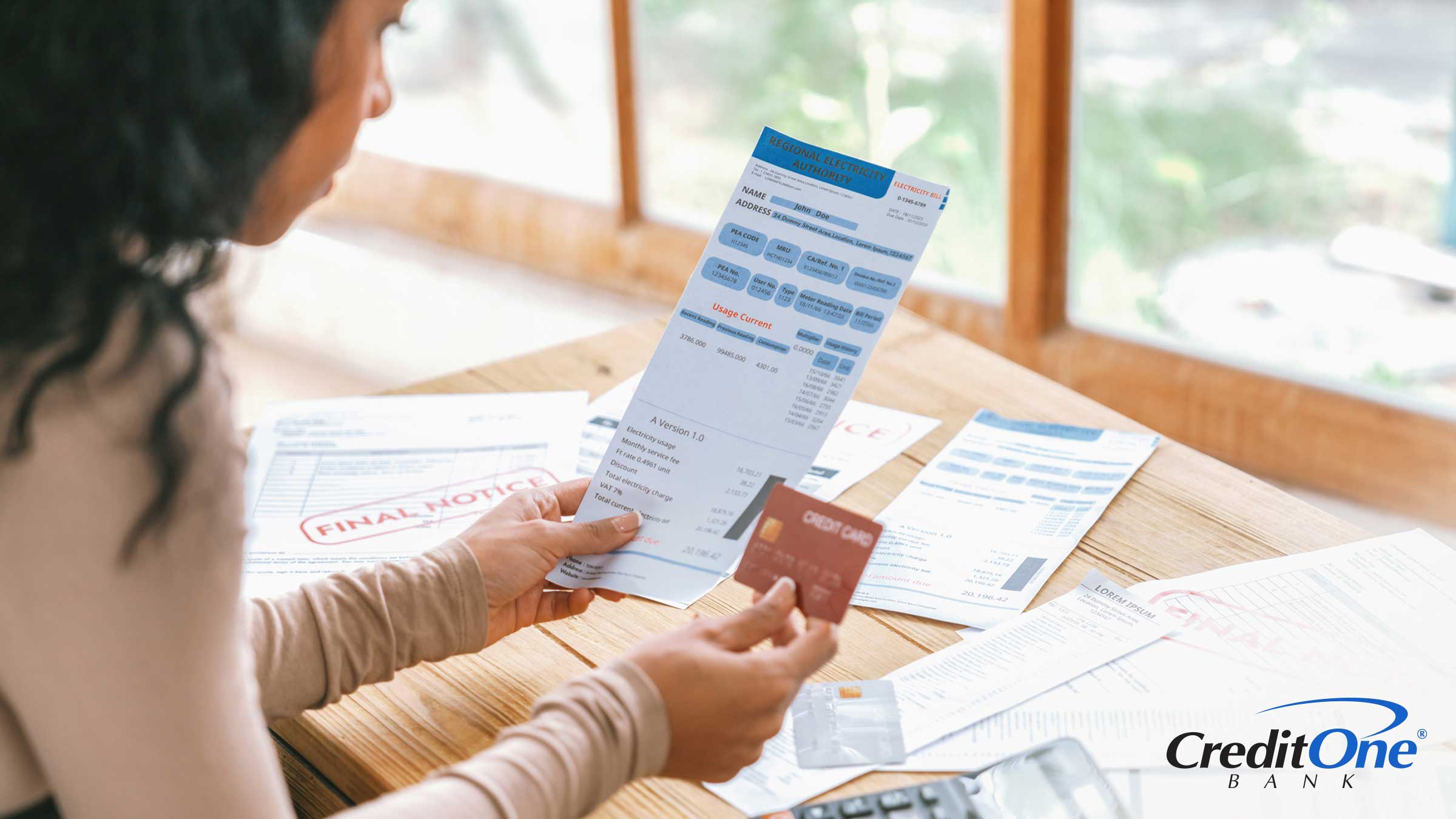 A young woman looks at her credit card and several past-due invoices, indicating her credit card may be charged off.