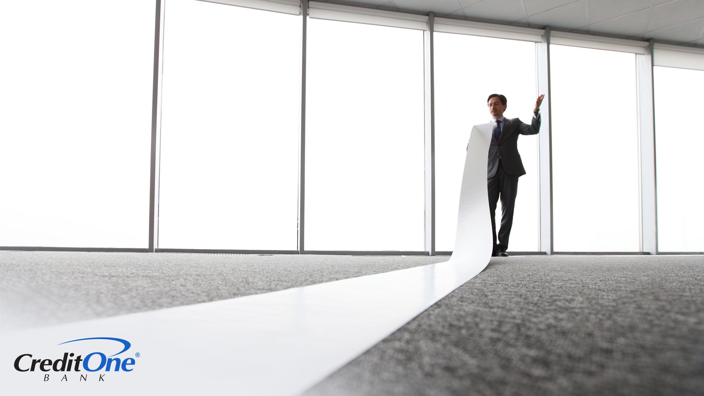 A businessman in an office holds the end of a long and flowing paper report, wondering how the length of his credit history impacts his credit score.