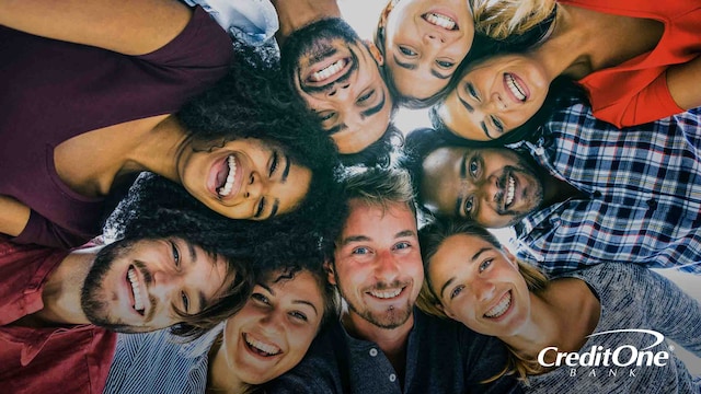 A diverse friend group of millennials gathers in a huddle, smiling happily while considering how credit scores affect their social status.
